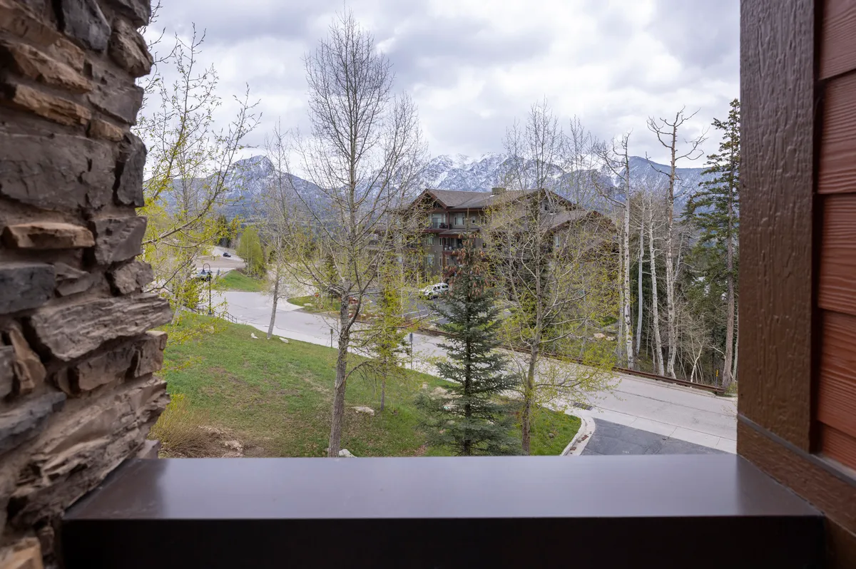 A serene view of a mountain range framed by aspen trees, with a meandering road drawing the eye into the scenic distance. A neighboring building hints at resort life but the focus remains on natural beauty and open space.