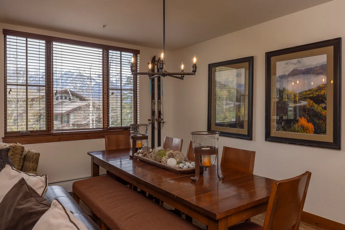 This image showcases a dining table set beneath a stylish chandelier, positioned next to a window that frames a scenic outdoor view. Framed artwork adorns the walls, adding to the inviting atmosphere ideal for shared meals and celebrations.