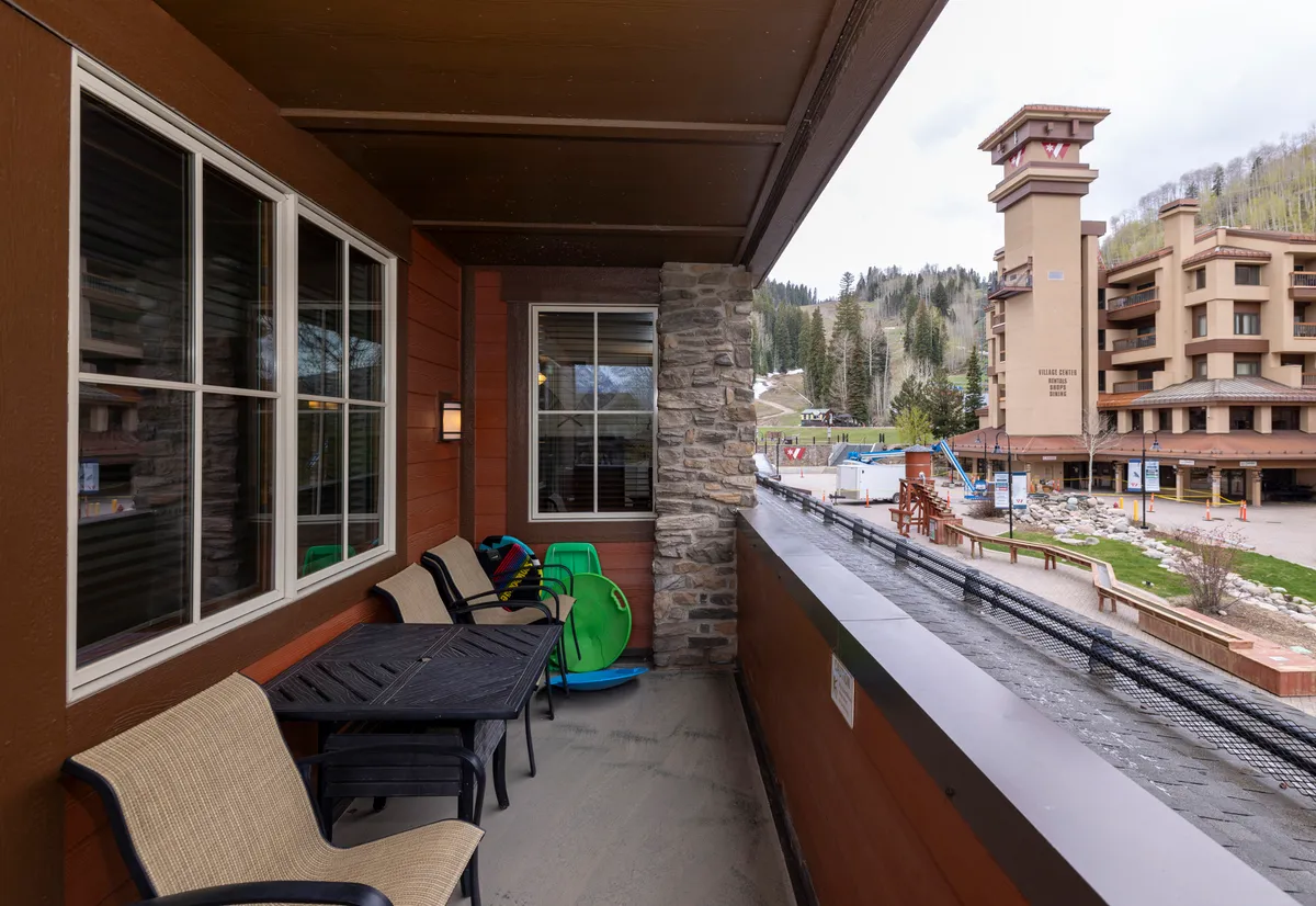 This exterior image features a private balcony outfitted with comfortable seating, offering unobstructed mountain views. An adjacent lodge building is visible, further setting the scene of a mountain retreat. The space exudes tranquility, perfect for morning coffee or evening toasts while soaking in the stunning landscape.