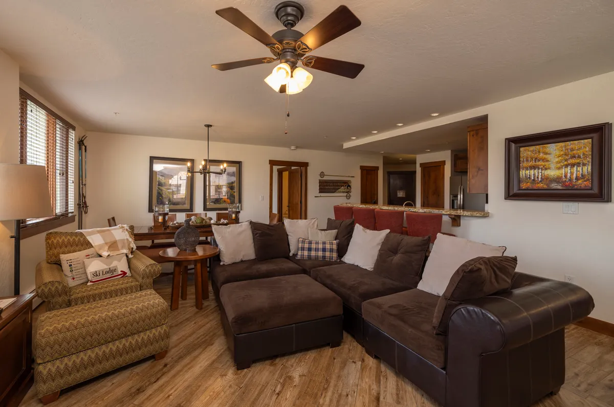 A spacious dining area with a large sectional sofa, a generous dining table set for a meal, decorative artwork, and warm lighting. The mood is inviting, encouraging family gatherings, entertaining, and sharing meals together.