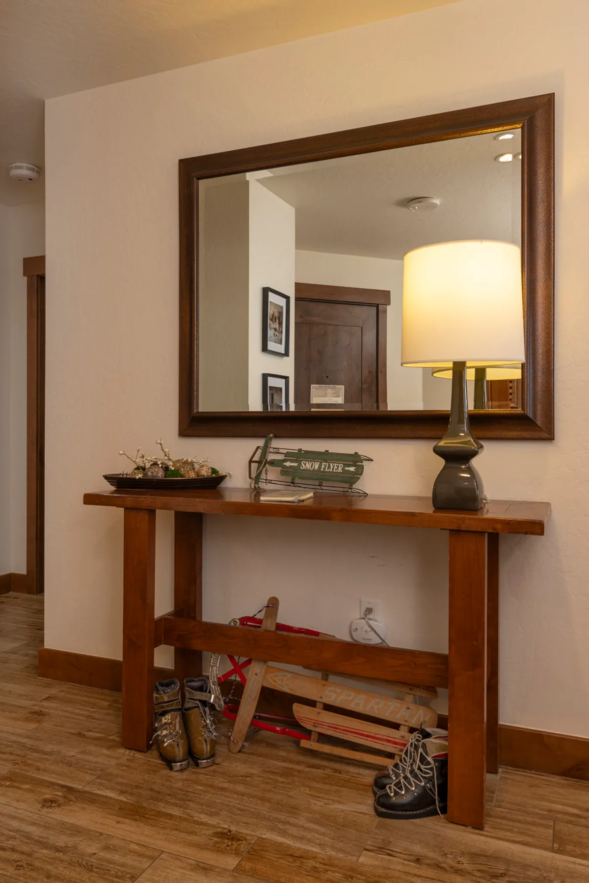 This image shows the welcoming entryway of the condo, featuring a wooden console table with decorative items, a large mirror, and ski equipment neatly stored to the side. The setting conveys a sense of arrival and readiness for outdoor adventure, with the ski gear hinting at year-round recreational pursuits.